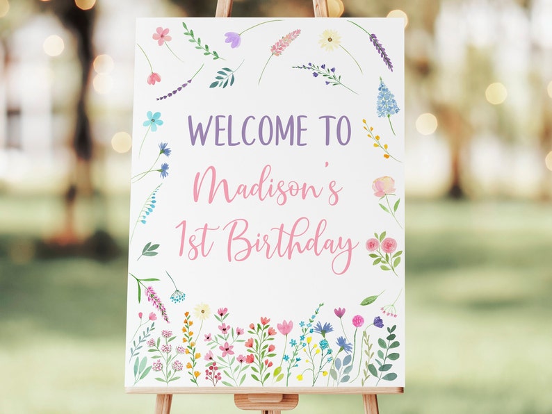 Puede incluir: Un cartel de bienvenida blanco con un borde floral. El cartel dice "Bienvenido a Madison's 1st Birthday" en letras rosa y morado.