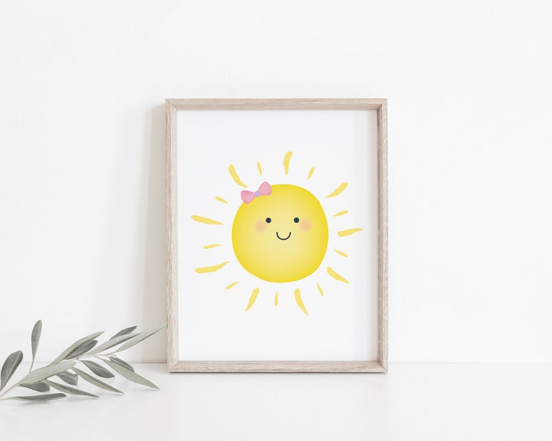 Puede incluir: Una impresi&oacute;n enmarcada de un sol amarillo con un lazo rosa, sonriendo con mejillas sonrosadas. El sol tiene rayos amarillos que irradian de &eacute;l.