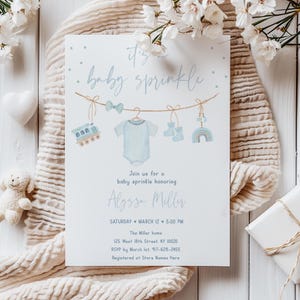 May include: A baby sprinkle invitation with a light blue theme. The invitation features the text "baby sprinkle" and illustrations of baby clothes and toys. The invitation includes the name Alyssa Miller, date, time, and address.