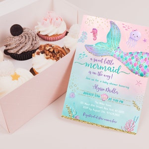 May include: A baby shower invitation with a mermaid tail design in shades of pink, purple, and teal with gold glitter accents. The text reads "a sweet little mermaid is on the way!" and includes details for the event, such as the date, time, and location.