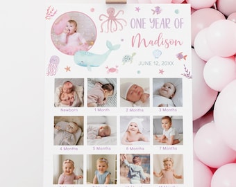 May include: A one-year photo display featuring a collage of baby photos. The design includes a pink and purple color scheme with sea-themed illustrations and the text "ONE YEAR OF Madison JUNE 12, 20XX". The display is on an easel.