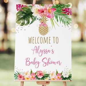 May include: Welcome to Alyssa's Baby Shower sign with a tropical theme. The sign features a gold pineapple, pink and white flowers, and green leaves. The background is white with gold glitter.