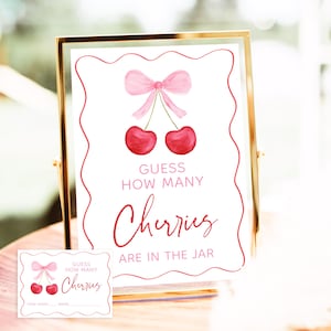 May include: A pink and white sign with a pink bow and two red cherries. The sign says "Guess how many cherries are in the jar".