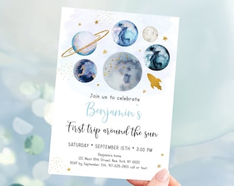 May include: A white invitation card with a watercolor design of planets and gold stars. The text reads "Join us to celebrate Benjamin's First trip around the sun" with event details. A gold rocket is also featured.