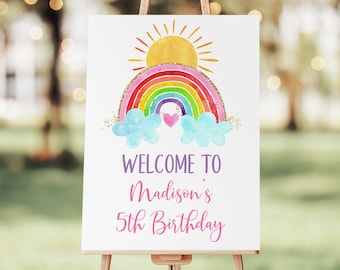 May include: Welcome to Madison's 5th Birthday sign with a rainbow, sun, and clouds. The rainbow is multi-colored with gold glitter accents. The sun is yellow and the clouds are light blue.