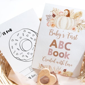 Peut inclure: Un livre d'images ABC pour bébé avec une illustration de beigne pour la lettre D. La couverture présente une citrouille aquarelle avec des feuilles d'automne et le texte "Baby's First ABC Book Created with love".