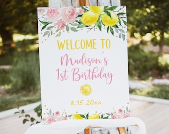 May include: Welcome to Madison's 1st Birthday sign with pink and yellow watercolor flowers, lemons, and gold glitter. The date 8.15.20xx is printed below the text.