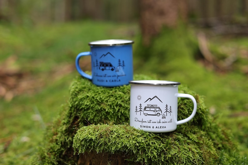 May include: Two enamel camping mugs with a camper van design. The blue mug says "Draufan ist wo ich sein will Rudi & Carla". The white mug says "Draufan ist wo ich sein will Simon & Alexa".
