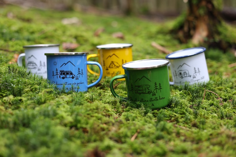 May include: Five enamel camping mugs with different designs and colours. The mugs feature a camper van and trees. The text on the mugs reads "Choose it, love it, pack it, drive it, camp it" and "Adventure starts here".