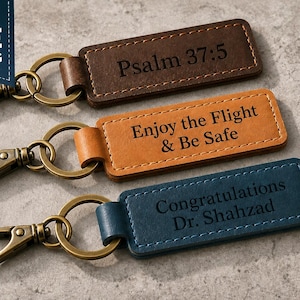 May include: Three rectangular leather keychains with antique brass lobster clasps and split rings. The top keychain is dark brown with the text Psalm 37:5, the middle is tan with Enjoy the Flight & Be Safe, and the bottom is blue with Congratulations Dr. Shahzad.