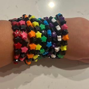 May include: A stack of colorful star-shaped bracelets with black beads. The bracelets are made of plastic and are worn on a person's wrist.