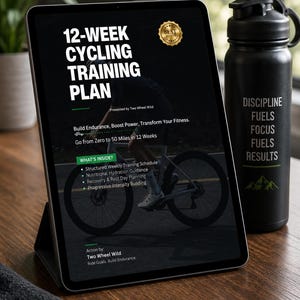 May include: A tablet displaying a 12-week cycling training plan with white text on a black background, featuring a cyclist graphic and the text 'Discipline Fuels Focus Fuels Results' on a black water bottle standing next to the tablet.
