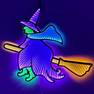 May include: A neon Halloween decoration of a witch on a broomstick. The witch is wearing a purple dress and hat, with green skin and shoes. The broom is yellow. The decoration is lit with purple, green, and yellow lights, creating a vibrant display.