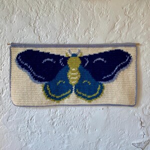 May include: A crocheted wall hanging featuring a blue and green butterfly with yellow accents.