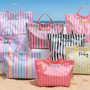 Peut inclure: Une collection de huit sacs fourre-tout rectangulaires à rayures verticales de différentes couleurs, chacun doté de deux poignées supérieures et d'un nom personnalisé brodé sur le devant, incluant les noms Londyn, Reese, Brielle, hadley, Sienna, Melody, Finley et MORGAN.