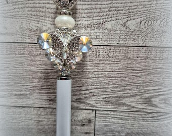 May include: A silver pen with a crystal butterfly design and a crown-shaped top. The pen is on a white surface with the text "Aunt Mannys Creations".
