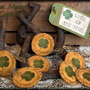 Puede incluir: Una colección de ocho posavasos redondos de tela amarilla con diseños de trébol verde. Los posavasos están dispuestos alrededor de ganchos de metal oxidado. Un letrero dice "Luck of the Irish".