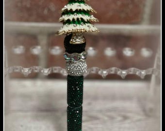 May include: A green and white Christmas tree-shaped pen with rhinestones. The pen is decorated with a black and white bow and has a green glitter barrel.