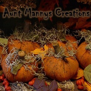 May include: Handmade orange pumpkins with green stems and moss detailing. The pumpkins are displayed with autumn leaves and a tag reading "Olde Tyme Harvest". The text "Aunt Mannys Creations" is visible at the top of the image.