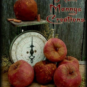 Può includere: Una natura morta rustica con mele rosse e bastoncini di cannella. Una mela poggia su una bilancia vintage, mentre altre sono raggruppate sotto. L'immagine include il testo "Aunt Manny's Creations".