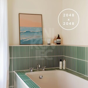May include: A white bathtub with green tile surround. The tile is arranged in vertical stripes. A framed print of a seascape hangs above the tub. There are bottles of toiletries on a shelf above the tub.
