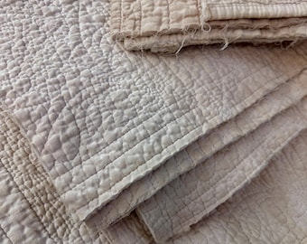 Puede incluir: Primer plano de una tela acolchada de color beige claro. La tela tiene un patrón texturizado y en relieve con líneas cosidas y un borde doblado. La apariencia general es suave y vintage.