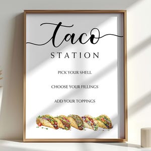 May include: A framed print with the words "Taco Station" in elegant script. Below, it lists "Pick Your Shell," "Choose Your Fillings," and "Add Your Toppings." A watercolor illustration of tacos is at the bottom. The frame is gold.