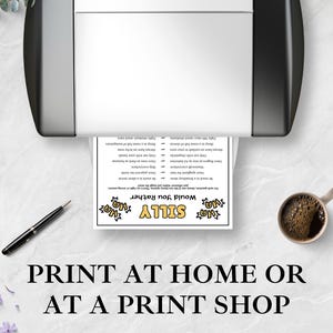 May include: A white paper sheet featuring a Silly Would You Rather game with black text and yellow accents, emerging from a black and white printer. A black pen and a ceramic mug filled with dark coffee are placed on the white marble surface.