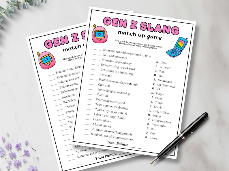 May include: Two white sheets of paper with the text "GEN Z SLANG match up game" printed in black, pink, and blue. The game includes a list of Gen Z slang terms and their definitions. A black pen rests on the bottom right corner.