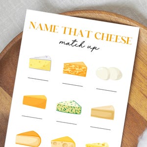 May include: A white card with the text "NAME THAT CHEESE match up" in gold lettering. The card features illustrations of various cheeses with blank lines below each for matching. The card is on a wooden tray.
