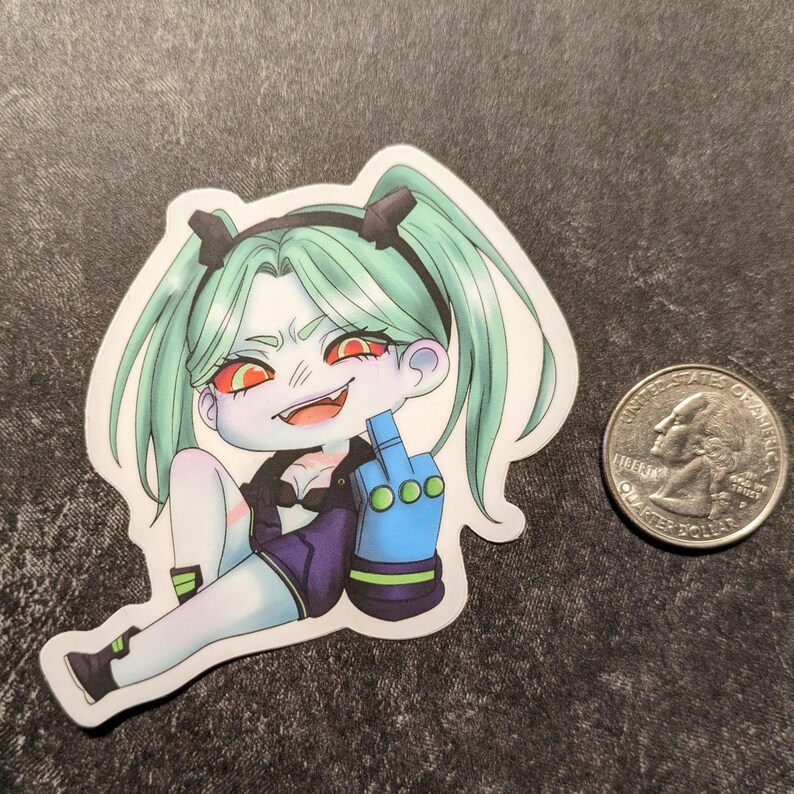 May include: A sticker featuring a cartoon character with mint green hair in pigtails, red eyes, and a blue glove giving the middle finger. The character is wearing a black jacket and purple shorts. A US quarter is next to the sticker.
