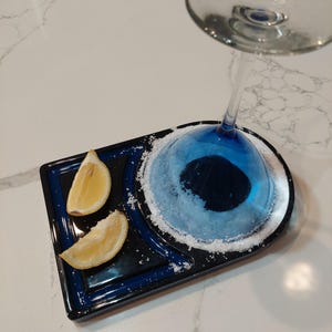 May include: A blue and black ceramic tray with a rim of salt around a martini glass. Two lemon wedges are on the tray.