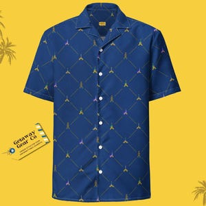 May include: A blue short-sleeved button-down shirt with a repeating pattern of Eiffel Towers in various colors. The shirt has a collar and a pocket on the left side. The text "Getaway Gear Co." is on a tag attached to the shirt.
