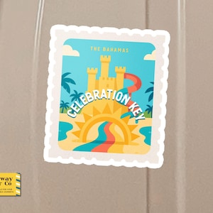 Op de afbeelding: Een sticker met een kleurrijke illustratie van een zandkasteel met een rode glijbaan, palmbomen en een zon boven water. De tekst luidt "The Bahamas" en "Celebration Key". De sticker heeft een witte, postzegelachtige rand.