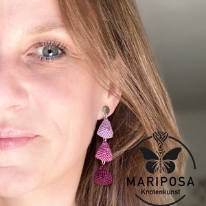 Könnte beinhalten: Ein Paar lange, baumelnde Ohrringe mit drei dreieckigen Perlen in Violett- und Rosatönen. Die Perlen sind aus geknüpfter Schnur gefertigt und an einem silbernen Haken befestigt.