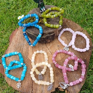 May include: Seven bracelets made of square-shaped beads in various colours, including blue, green, pink, and white. Each bracelet has a silver charm attached to it.