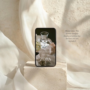 May include: A black smartphone mockup with the word "ZORA" on the screen, resting on a textured, light-colored block. The screen displays a glass and floral arrangement. The text "MOCKUP COLLECTION" and dimensions are also visible. Soft, white fabric drapes in the background.