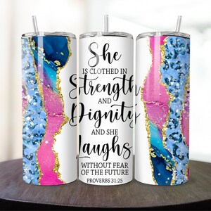 May include: A white tumbler with a pink, blue, and gold abstract design. The tumbler has a quote that reads "She is clothed in strength and dignity and she laughs without fear of the future. Proverbs 31:25."