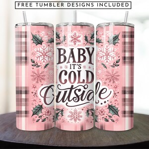 May include: Three pink and brown stainless steel tumblers with a plaid pattern and a winter-themed design. The tumblers feature snowflakes, holly, and the text "Baby It's Cold Outside".