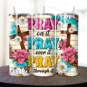 May include: Three stainless steel tumblers with a wood grain background and floral designs. The tumblers have the text "Pray on it Pray over it Pray through it" printed on them.