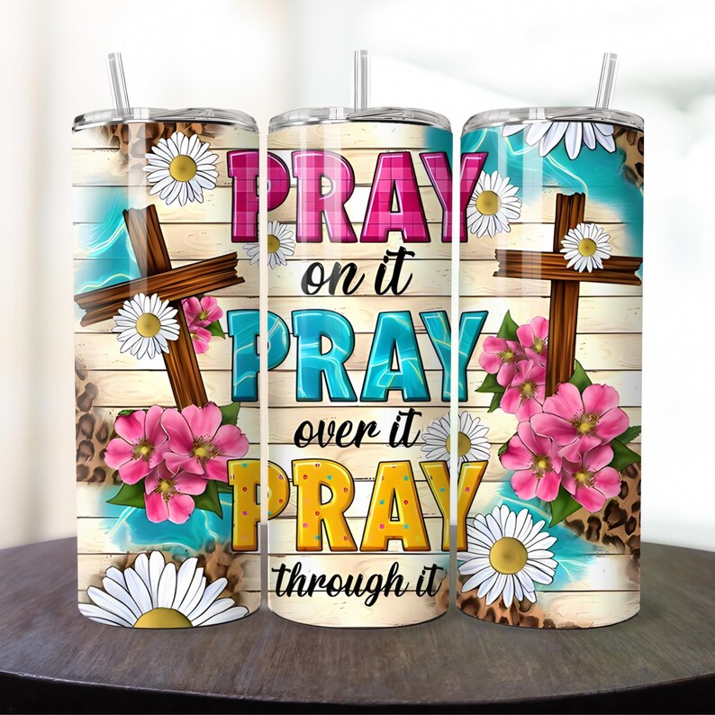 May include: Three stainless steel tumblers with a wood grain background and floral designs. The tumblers have the text "Pray on it Pray over it Pray through it" printed on them.