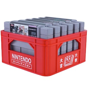 Może przedstawiać: Czerwona plastikowa skrzynia wypełniona szarymi kartridżami do gier Nintendo Super Famicom. Skrzynia ma logo Nintendo i japoński tekst. Kartridże są starannie ułożone w skrzyni.