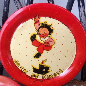 May include: Red metal plate with a white center featuring a cartoon illustration of a child jumping over a candle. The text "Jack Be Nimble" is printed on the plate.