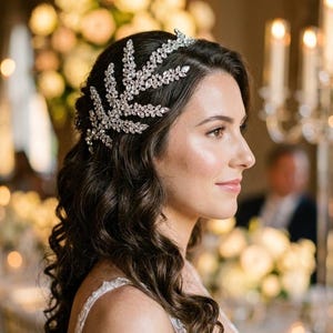 K&ouml;nnte beinhalten: Eine Frau mit dunklem, welligem Haar tr&auml;gt einen silbernen Kopfschmuck. Der Kopfschmuck hat ein blattartiges Design und ist mit klaren Kristallen besetzt. Die Frau tr&auml;gt ein wei&szlig;es Kleid, und der Hintergrund ist unscharf mit warmen T&ouml;nen.