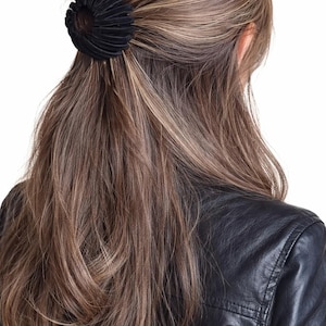 Könnte beinhalten: Ein schwarzes Scrunchie hält lange, wellige, braune Haare zurück. Das Scrunchie aus geripptem Stoff befindet sich am Hinterkopf. Die Person trägt eine schwarze Lederjacke.