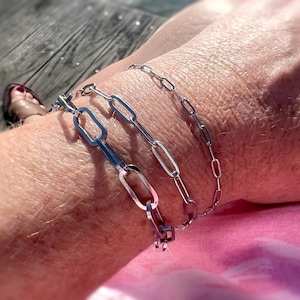 May include: Three silver chain bracelets with different link sizes. The bracelets are stacked on a person's wrist.
