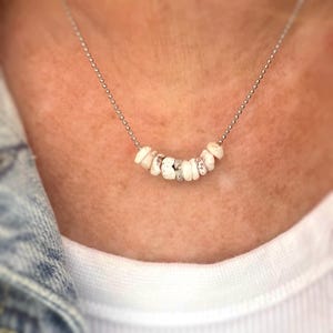 May include: A silver chain necklace with a row of white and grey shell beads.
