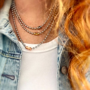 May include: A layered silver chain necklace with three gold and rose gold accent beads.