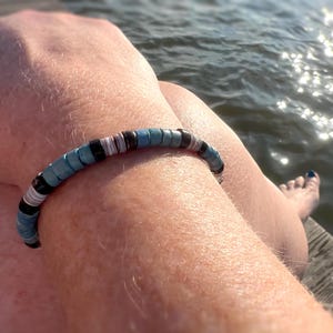 May include: A blue, white, and black beaded bracelet with a simple design. The bracelet is worn on a person's wrist.