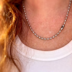 May include: A silver ball chain necklace with a lobster clasp closure.